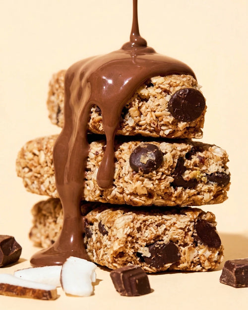 Close-up of a Bountiful Coconut Choc bar stack drizzled with melted chocolate, surrounded by coconut and chocolate pieces