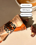 My Goodness Fudgy Choc n' Hazelnut bar broken in half next to a cup of coffee, showing its rich chocolate texture