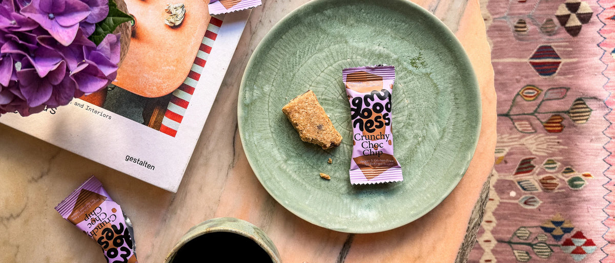 My Goodness Crunchy Choc Chip snack bar styled on a green plate with fresh flowers and a woven rug